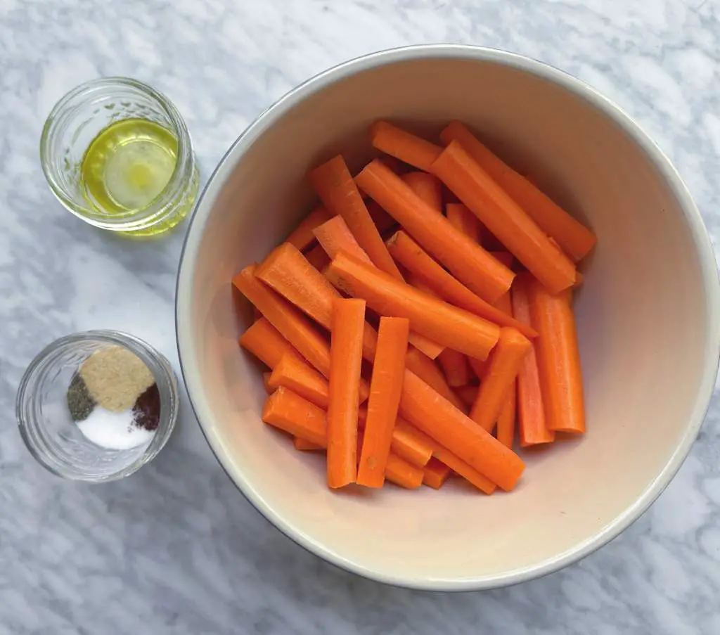 Chopped carrots in a bowl with small bowls of olive oil and spices