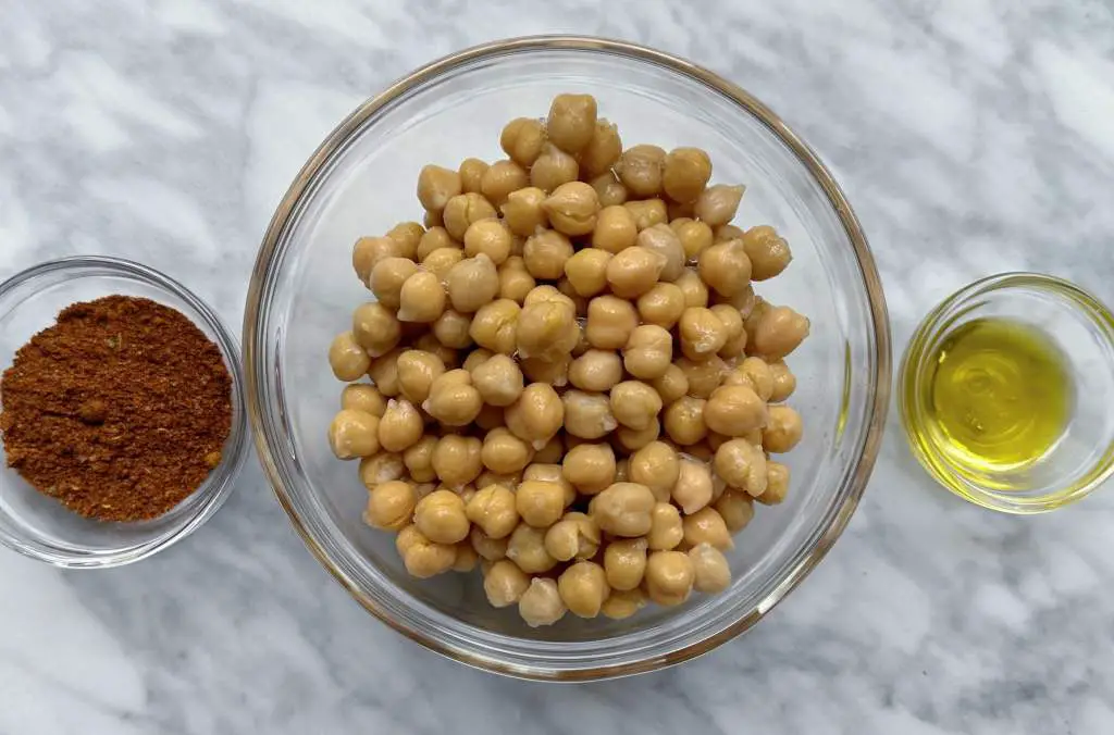 Chickpeas, taco seasoning and olive oil in individual bowls on a white marble surface