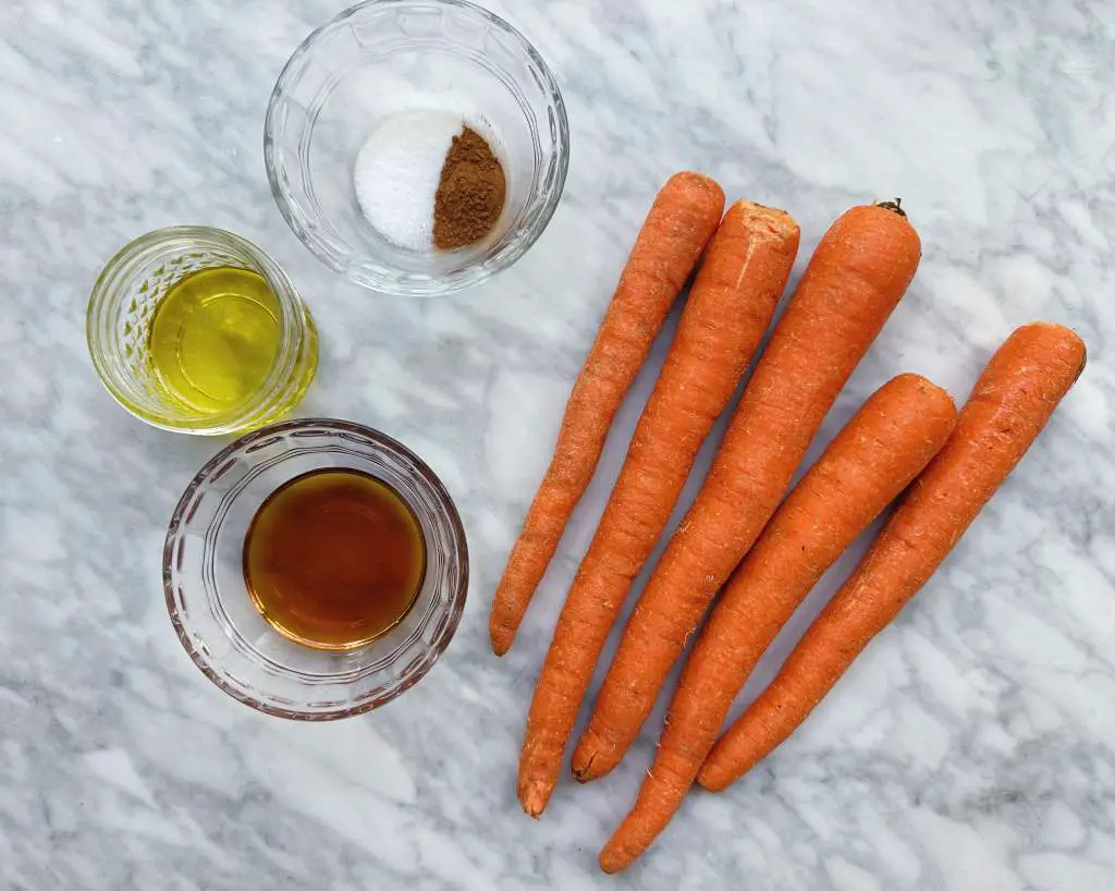 Carrots and small bowls of oil, spices and maple syrup on a white marble background