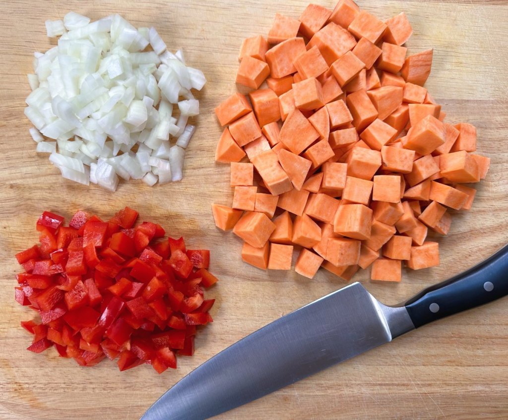 sweet potato, red bell pepper, and onion chopped on a cutting board next to knife