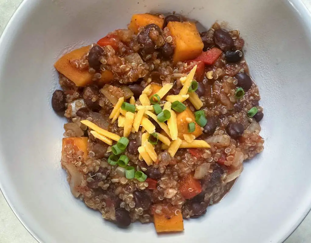 Bowl of quinoa chili topped with vegan cheddar cheese and chives