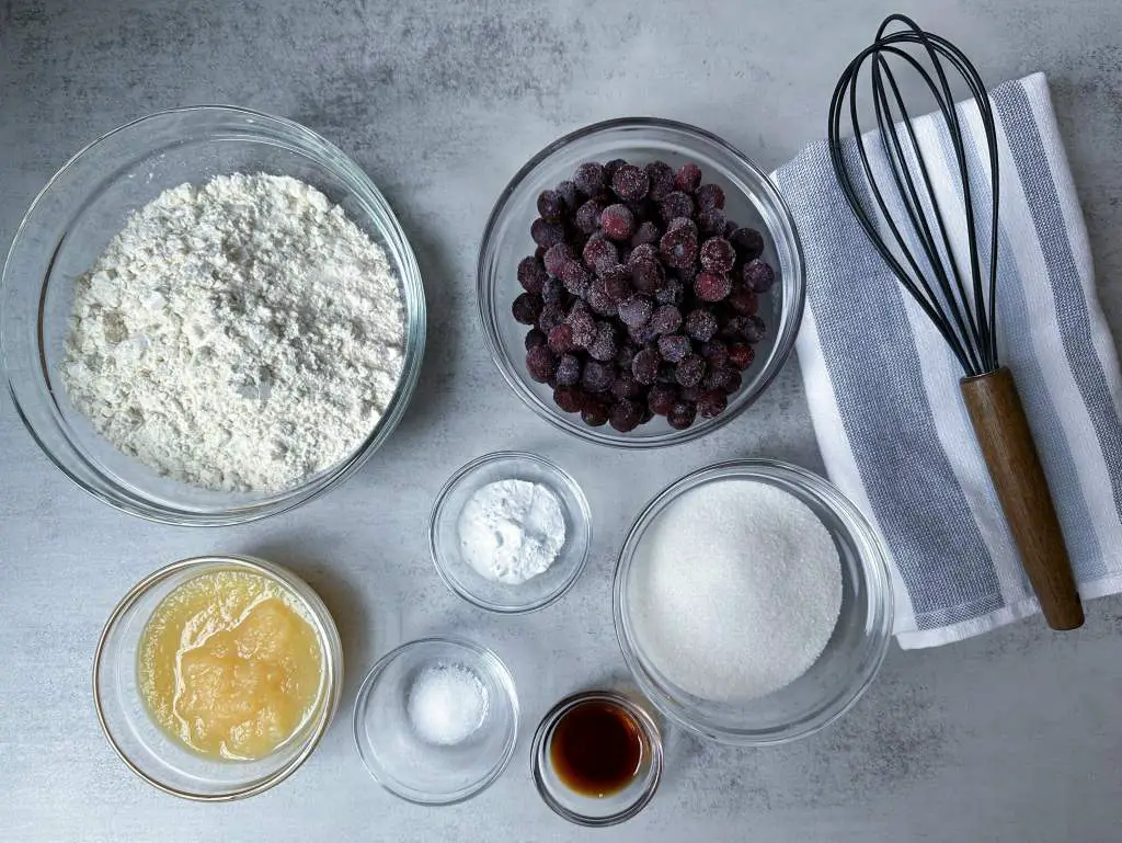 All ingredients for easy vegan blueberry muffins in separate bowls on a gray background