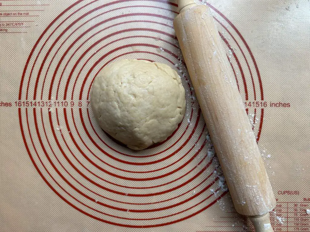 Finished ball of dough on a baking mat next to a rolling pin