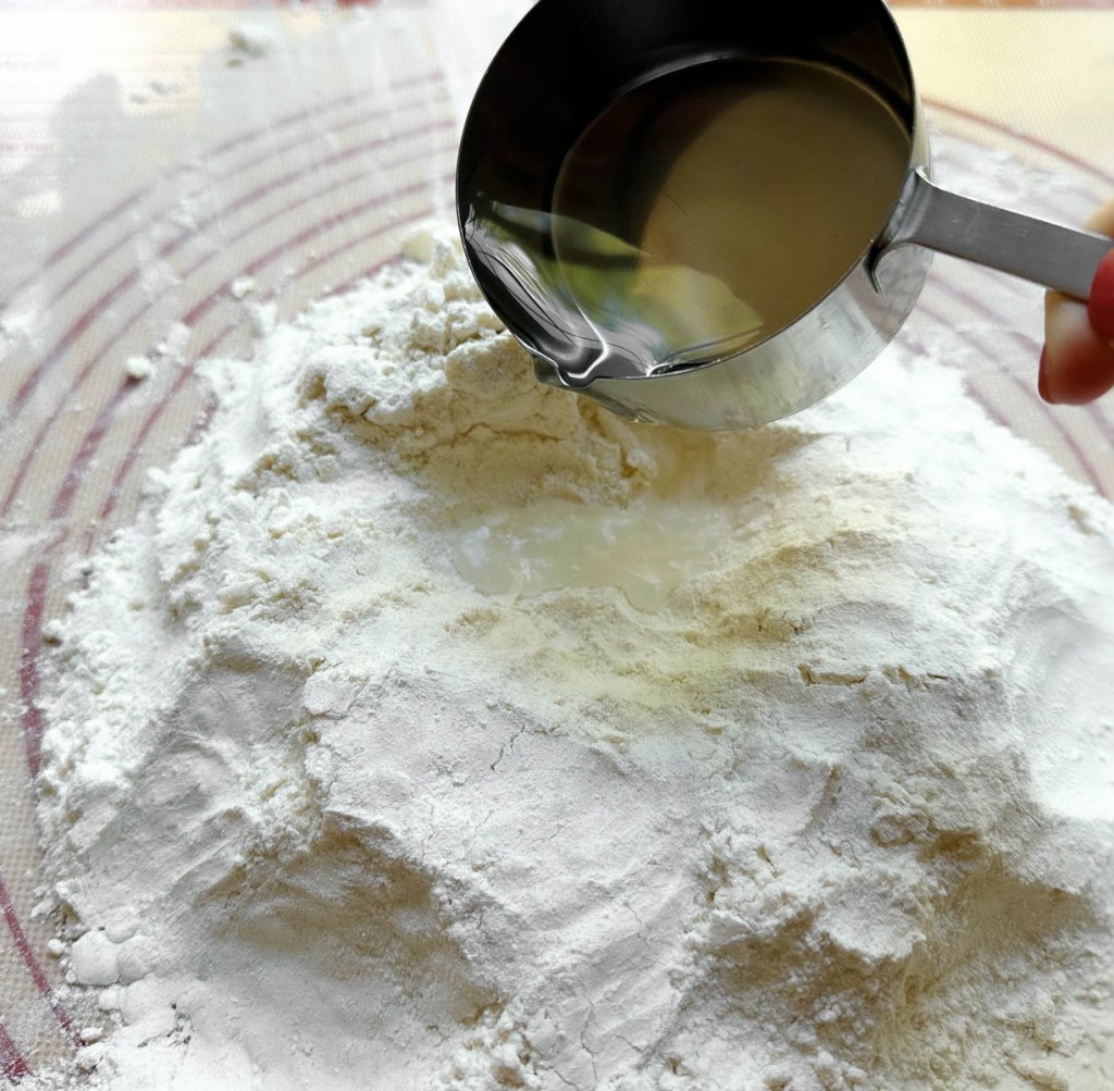 pouring water into a well made in flour mixture
