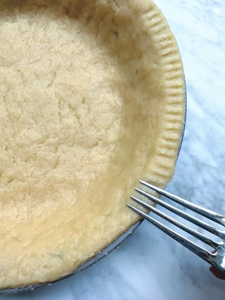 Pie crust made with vegan egg substitute, in tin with fork making marks around edge