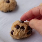 hand placing chocolate chip on top of ball of dough
