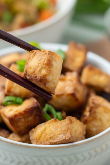 crispy sesame tofu close up being held by chop sticks