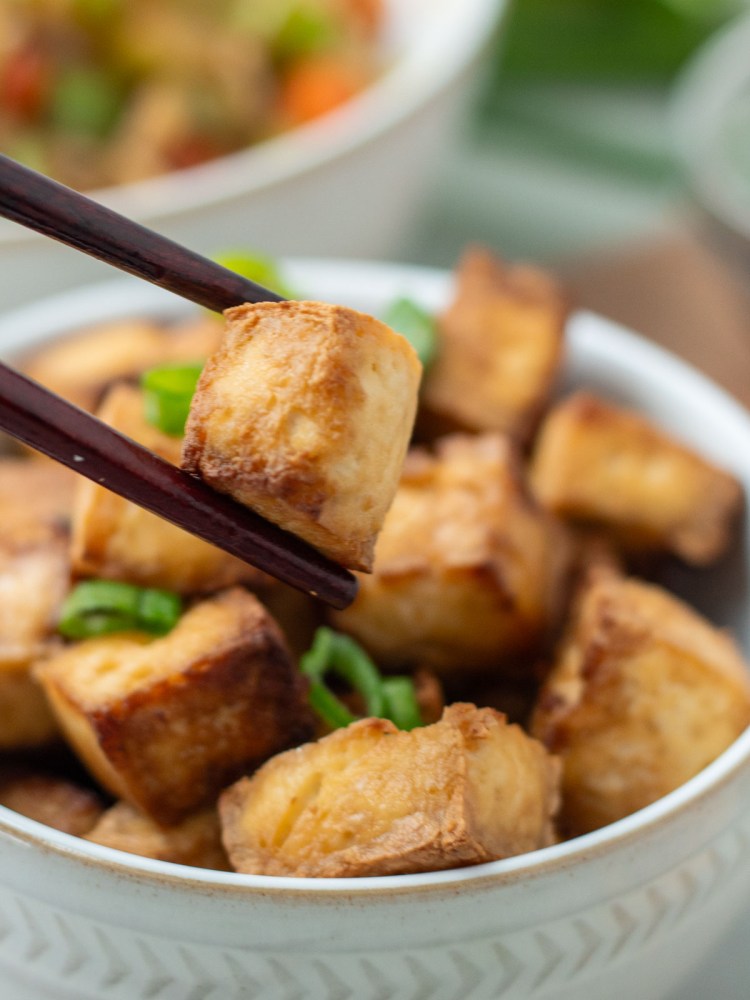 crispy sesame tofu close up being held by chop sticks