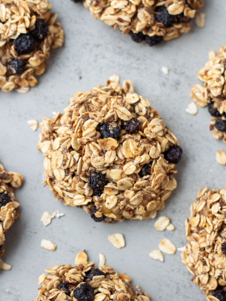 Finished healthy oatmeal cookies surrounded by oats on grey surface