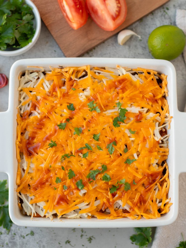 top view finished vegan mexican casserole garnished with enchilada sauce and herbs