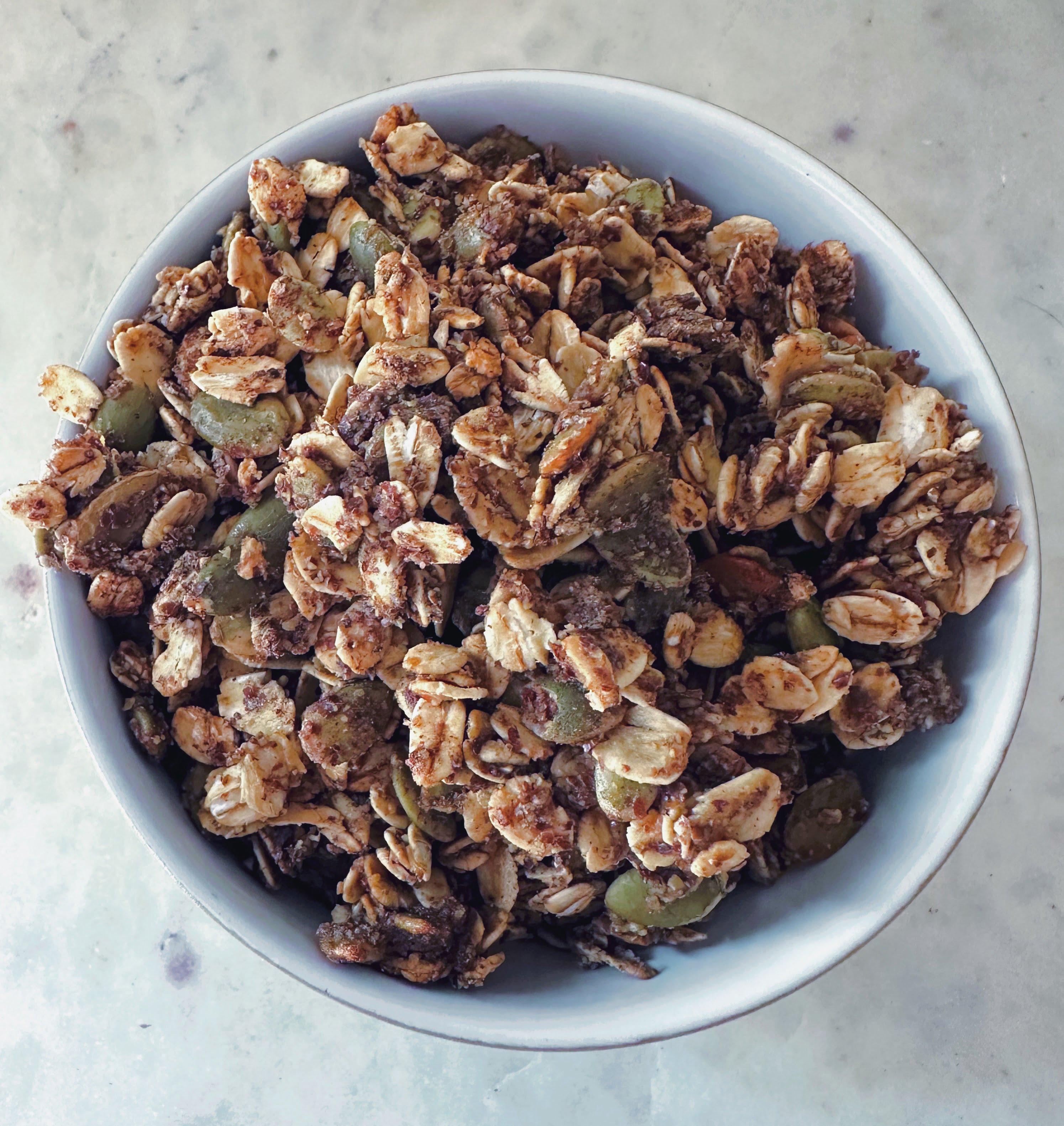 Bowl of pumpkin seed granola on a white marble background