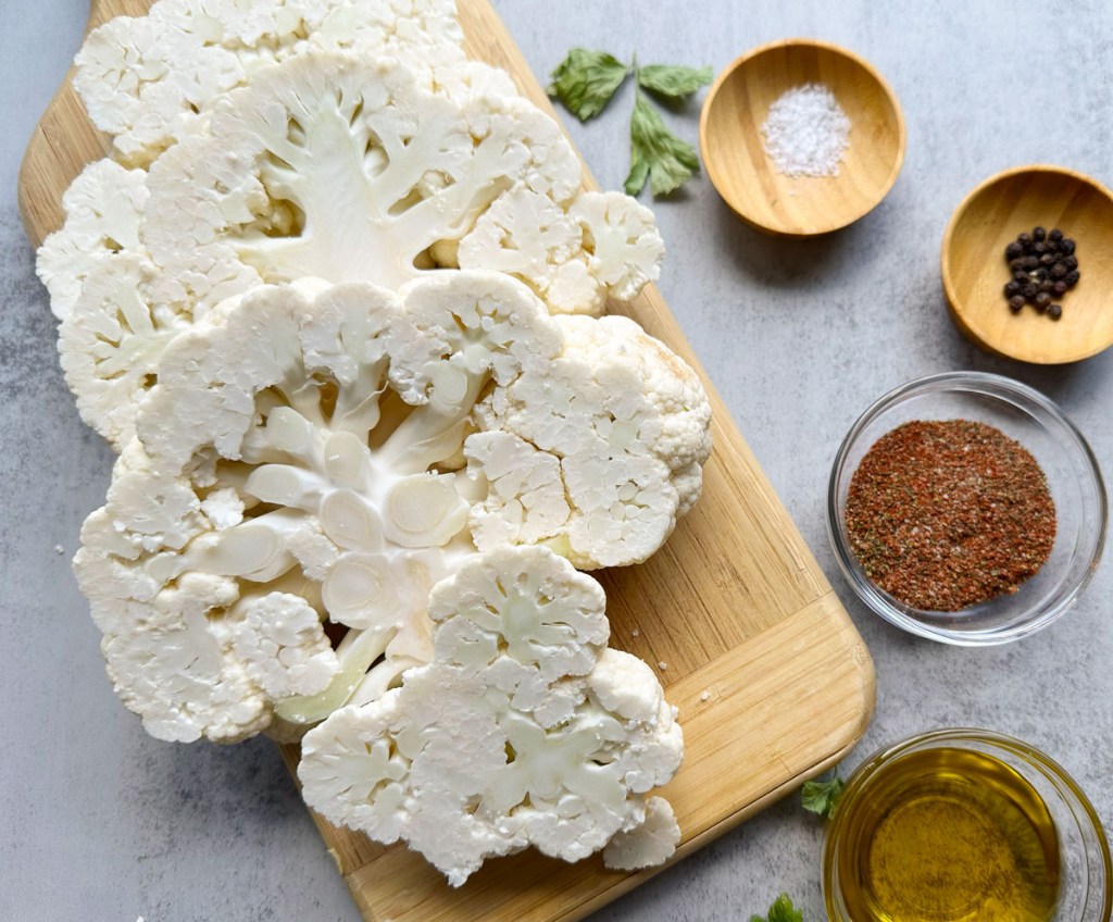 Cut cauliflower steaks and seasonings on a grey background