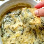 finished vegan spinach artichoke dip with pita chip scooping some out