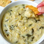 finished vegan spinach artichoke dip with pita chip scooping some out