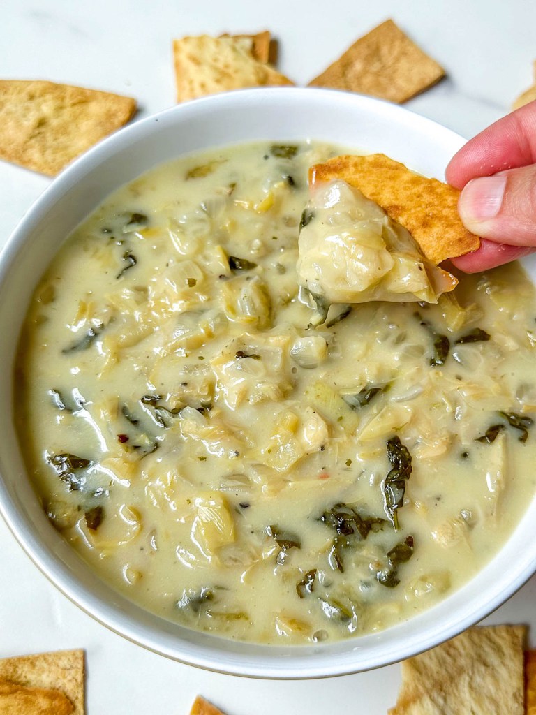 finished vegan spinach artichoke dip with pita chip scooping some out