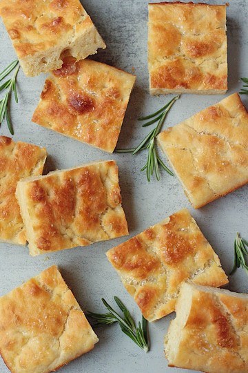 homemade vegan focaccia bread top view with herbs surrounding