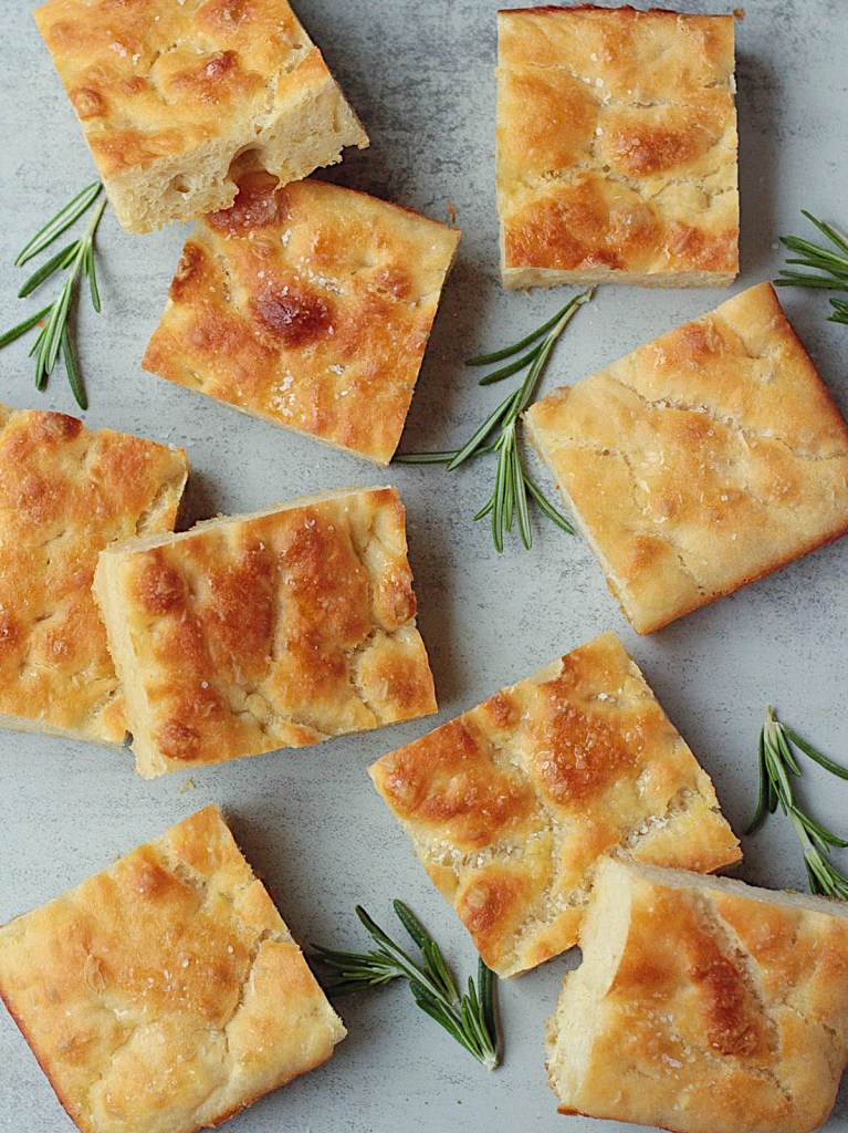 homemade vegan focaccia bread top view with herbs surrounding