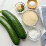 zucchini, breadcrumbs, spices and cornstarch on a white marble background. All ingredients needed for making air fryer zucchini fries.