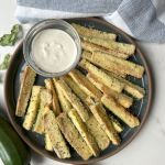 finished air fryer zucchini fries on a dark blue plate with a small bowl or ranch dressing