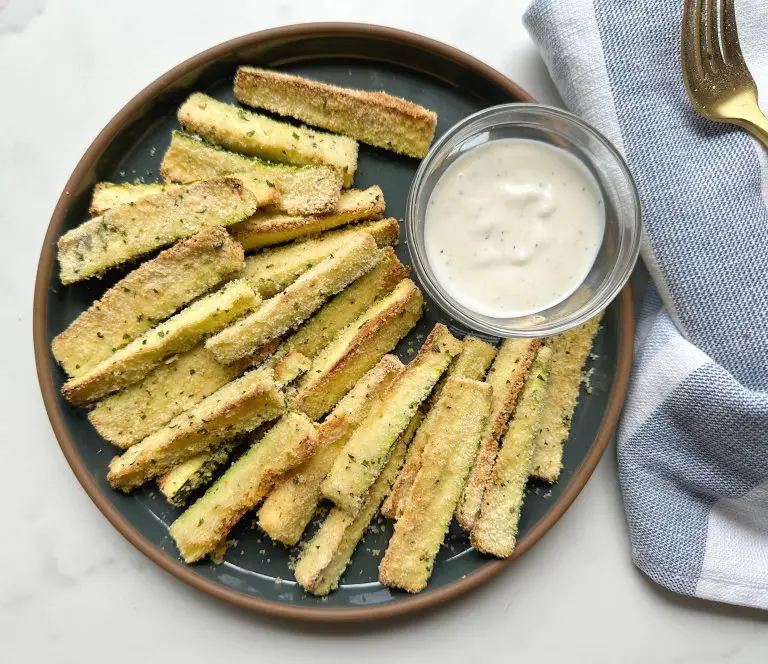 finished air fryer zucchini fries on a dark blue plate with a small bowl or ranch dressing