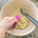 A toddler's hand is shaking sprinkles into the finished dough.