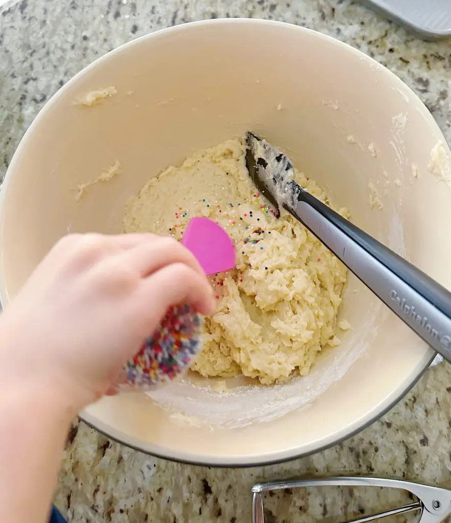 A toddler's hand is shaking sprinkles into the finished dough.