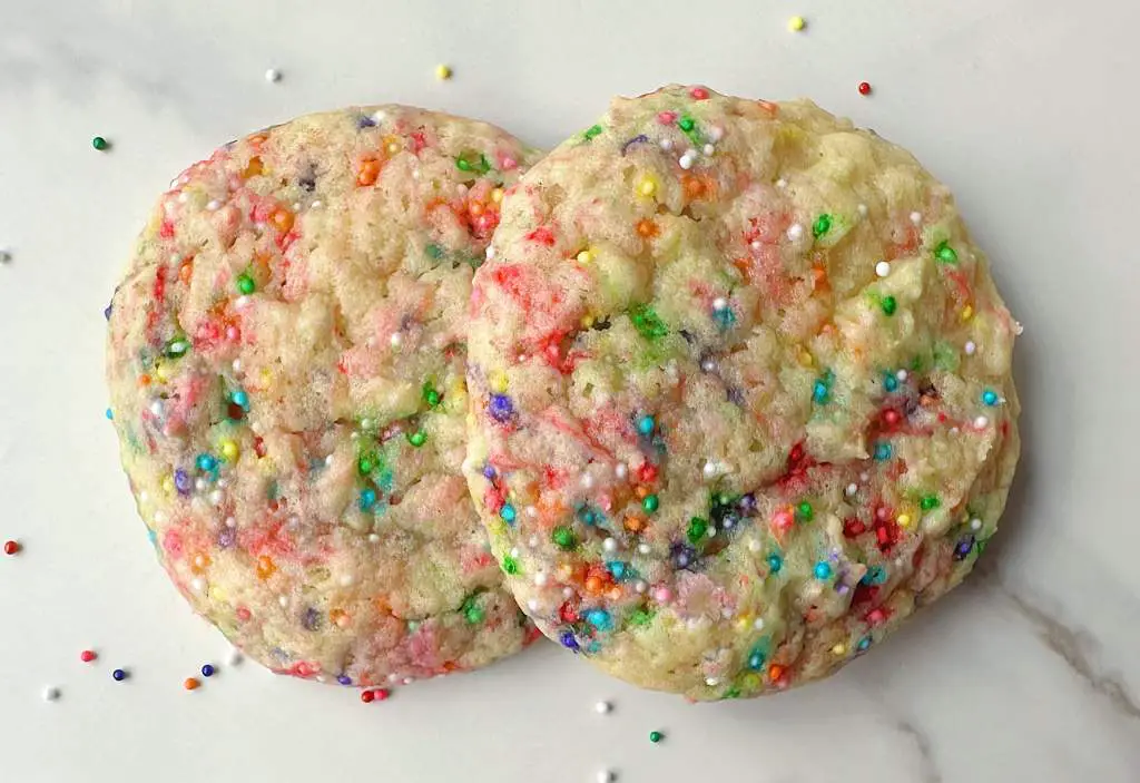 Vegan funfetti sugar cookies on a marble surface surrounded by sprinkles