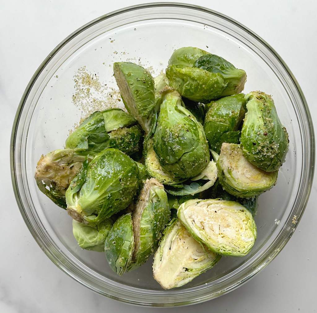 uncooked brussels sprouts coated in oil and spices in a glass bowl