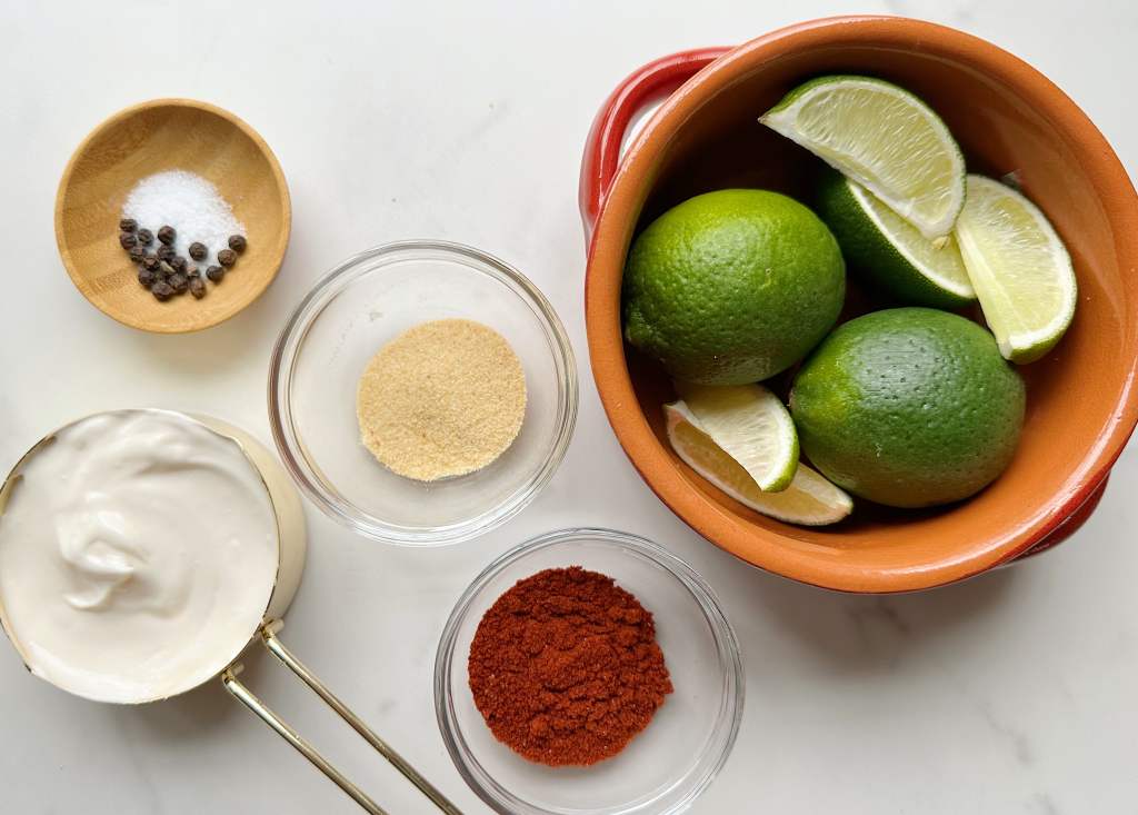Vegan mayo, salt, pepper, and spices next to a bowl of limes. All ingredients for vegan chipotle lime aioli