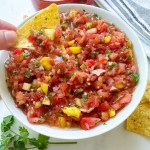 finished easy mango salsa with chip taking dip out of it