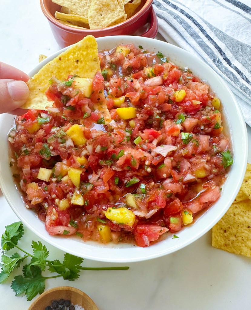 finished easy mango salsa with chip taking dip out of it
