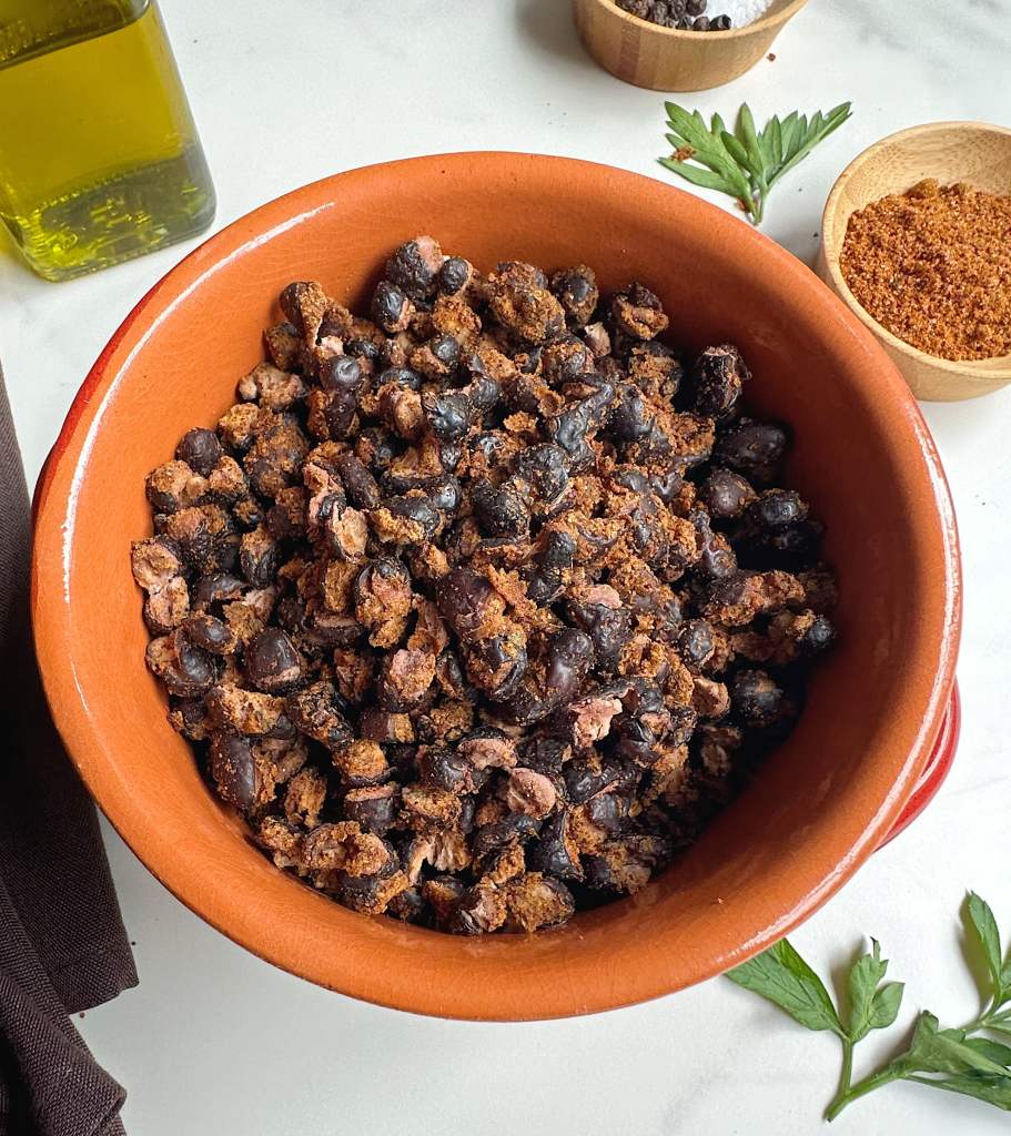 bowl of air fried black beans on a white background with spices in the back