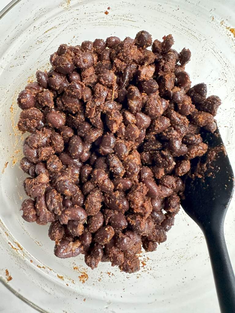 uncooked black beans coated in olive oil and spices in a glass bowl