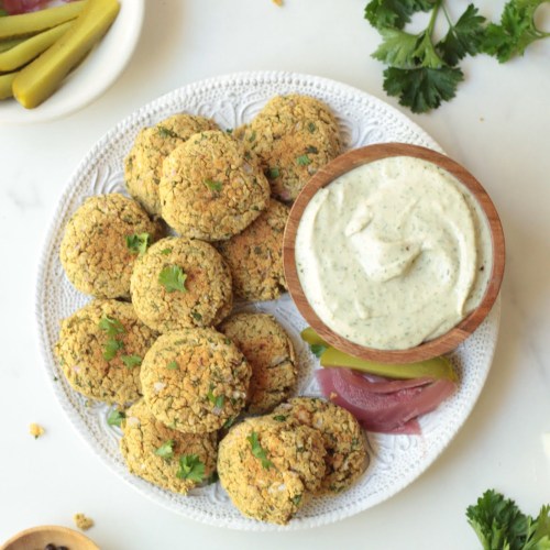 baked falafel on a white plate with a small bowl of garlic tahini dipping sauce