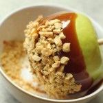 Vegan caramel apple being dipped in crushed peanuts