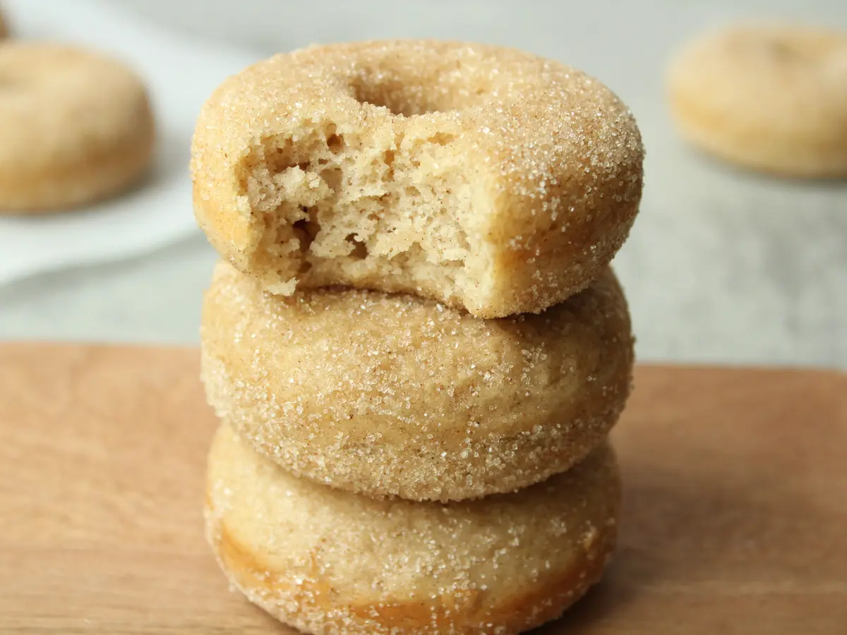 stack of 3 vegan cinnamon sugar donuts with a bit taken out of the top donut