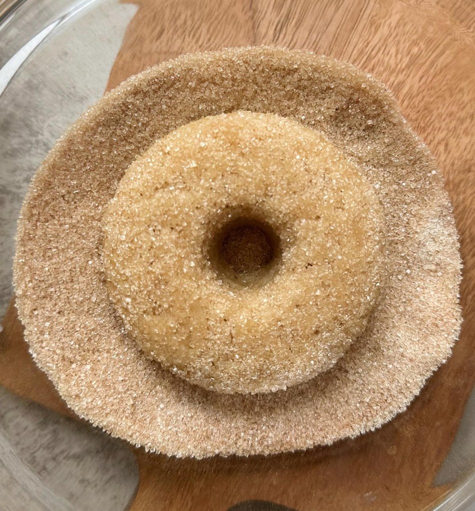 single vegan cinnamon sugar donut being coated in cinnamon sugar