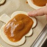 filled vegan mini pumpkin pie showing how to spread water around edge of puff pastry
