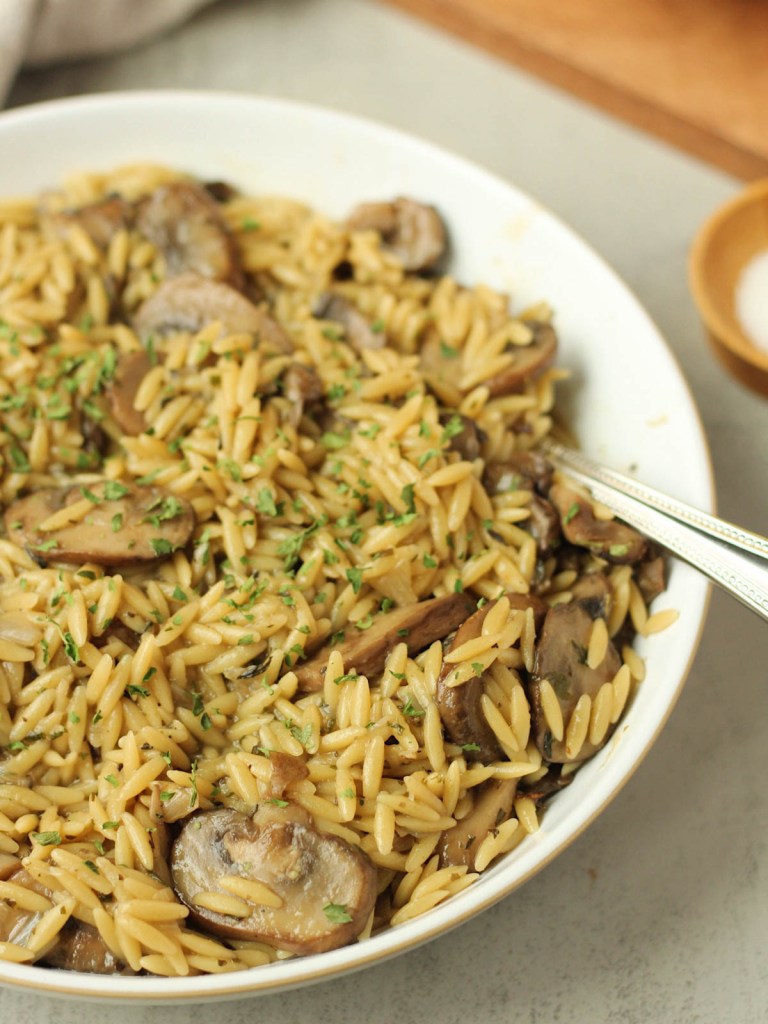 vegan mushroom orzo in a white bowl with silver spoon
