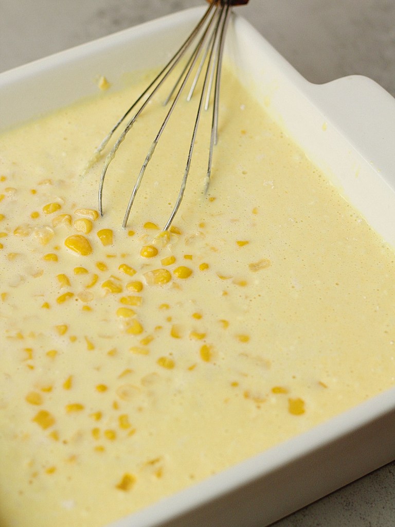 all ingredients in baking dish for vegan corn pudding with whisk