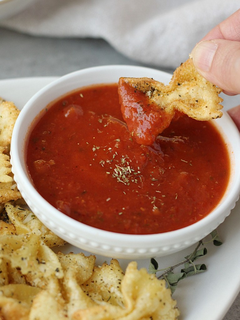 air fried pasta chip being dipped into marinara sauce