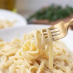 vegan fettuccine alfredo noodles wrapped around a gold fork
