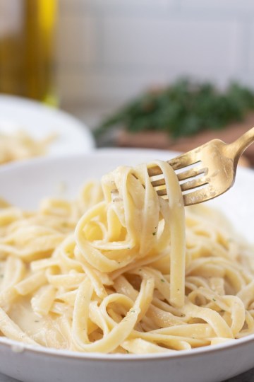 vegan fettuccine alfredo noodles wrapped around a gold fork