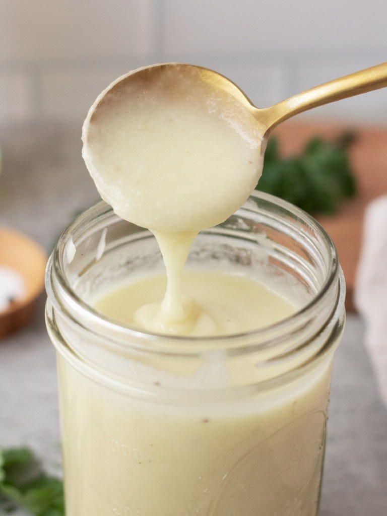 vegan alfredo sauce in a mason jar with spoonful showing consistency