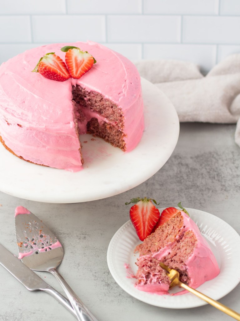 vegan strawberry cake frosted on cake stand with slice below