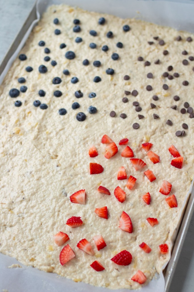 sheet pan filled with uncooked pancakes topped with strawberries, blueberries, chocolate chips