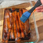 pastry brush brushing marinade on carrot strips in glass dish