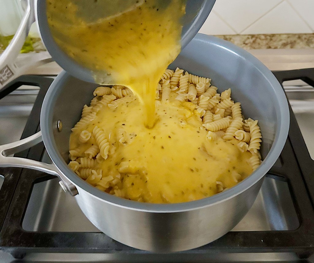 pouring vegan cheese sauce onto cooked noodles