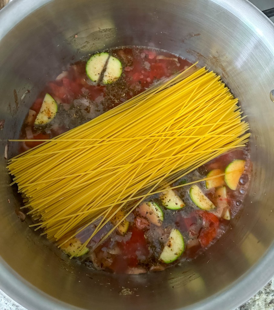 spaghetti noodles added into pot with veggies and boiling water